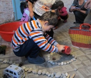 Pendant qu’il est accroupi, un enfant fait des cercles avec de petits cailloux et met du sable ou de la terre dans le cercle de cailloux.