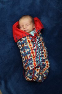Young baby in colorful moss bag.