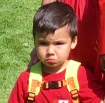 Close up of sad looking child standing in front of adult.