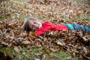 Smiling preschool child lying on pile of leaves.