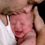 Adult cuddling very young crying baby.