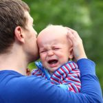 Parent holding and kissing head of crying baby.