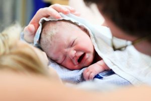 Newborn baby in towel on mother's chest.