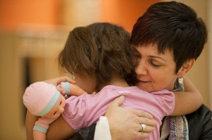 Adult hugs child holding doll.