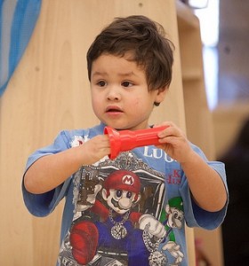 Makoonsag9 Preschooler gazing to their right with hand partially inside a cylindrical plastic toy.