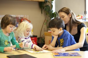 RRCpuzzle Une adulte assise à une table avec trois enfants d’âge préscolaire en train de faire un casse-tête.