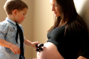 Young child touching abdomen of pregnant parent with toy.