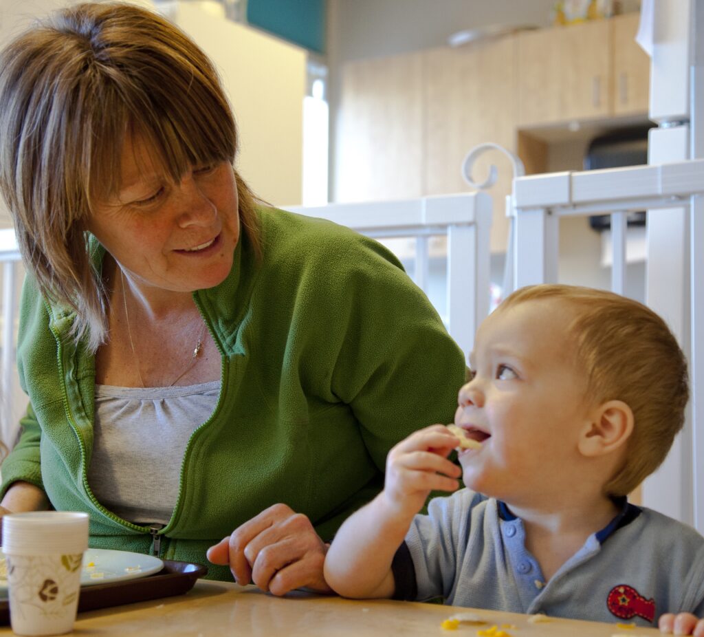 Smiling adult facing child eating snack.
